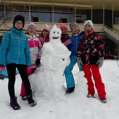 Mädchen stehen um einen Schneemann