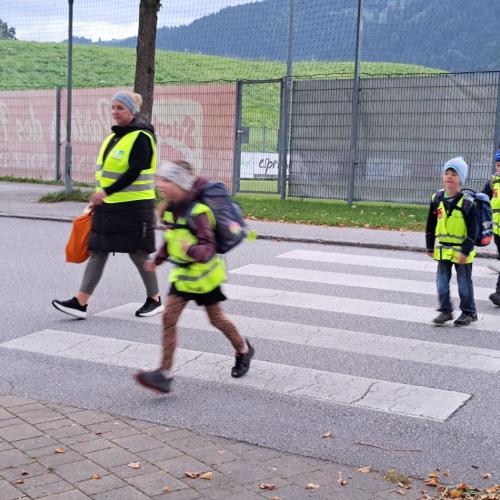 Kinder mit Warnweste gehen über den Zebrastreifen